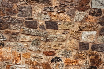 The texture of the stone wall, elements of brown, orange, gray and black. Original background, abstract pattern