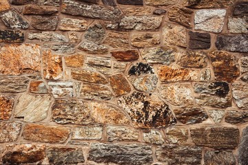 The texture of the stone wall, elements of brown, orange, gray and black. Original background, abstract pattern