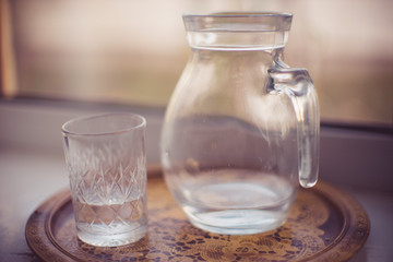 Jug of water and a glass in a tray on the windowsill