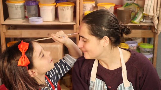 Young girl plays about. Paint her teacher's face at art workshop.
