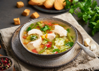 Homemade chicken soup with vegetables, broccoli on dark brown background, side view.
