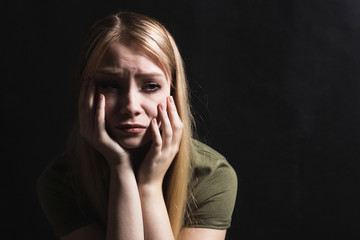 Sad young woman going to cry in a black background