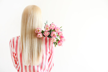 Obraz na płótnie Canvas Studio portrait of gorgeous young blonde woman with long straight hair wearing pink stripe crop top shirt, holding bouquet of many tender pink tulips. White isolated background, copy space, close up.