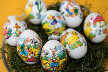 osterei mit eier bemalendem osterhase auf gelbem untergrund in nahaufnahme fotografiert zu ostern an einem sonnigen tag in farbe