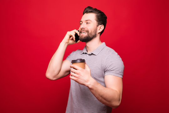 Handsome man with coffee cup to go talk on the phone isolated on red background