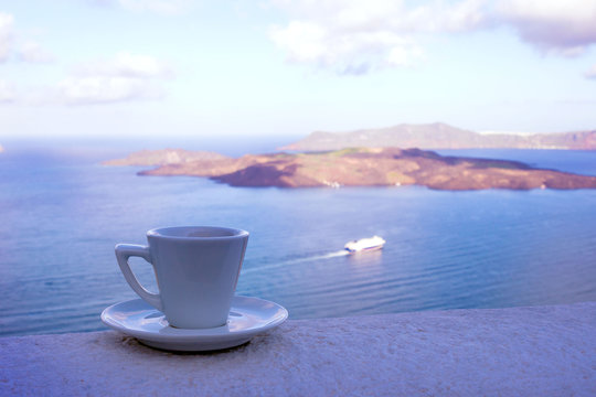 Strong delicious coffee in a white cup with a saucer against the backdrop of the sea and a floating liner. Great start to the day. Pleasant moments of life. Travel to Santorini, Greece.