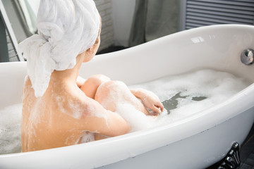 Fototapeta premium A young attractive girl relaxes in the bathroom and rests against the backdrop of a beautiful light interior. Spa treatments for beauty and health with skin care