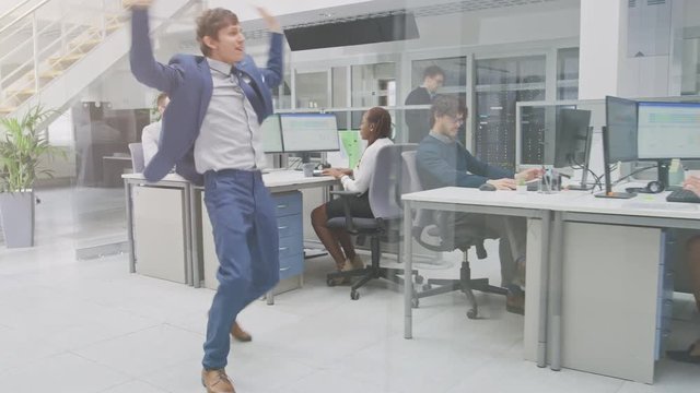 Young Fun Loving and Handsome Businessman Fooling Around, Dances Through the Open Space Office Hallway. Diverse and Motivated Business People Work on Desktop Computers