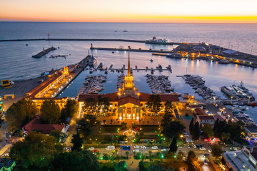 Aerial photography with quadrocopter. Sea port of Sochi with a bird's eye view. Evening illumination of the building. Yachts and boats are in the port. Resort town. Landmark. 