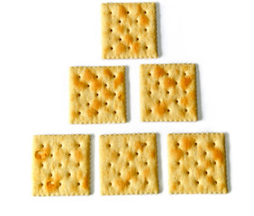 Six saltine crackers also known as soda and soup crackers on white, lined up in rows of one, two, and three as an educational counting concept.