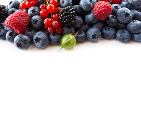 Ripe blueberries, red currants, backberries, gooseberries and raspberries on white background. Top view. Fruits and berries at border with copy space for text. Blue-black and red food.