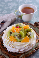 Delicious pavlova dessert as gentle, light, airy cake with meringue and cream with slices of orange and kiwi on top in a nice vintage wooden tray next to dessert fork on a linen napkin