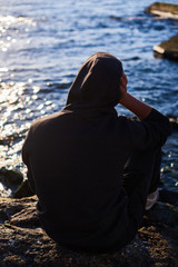 Man thinking while sitting on a rock and watching the ocean