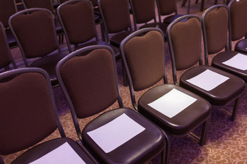 Brown chairs the conference hall before the event. First row for special guests. Empty places for your inscriptions on white paper sheets.