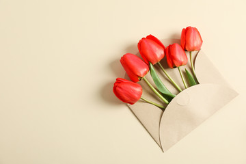 Envelope and beautiful red tulips with space for text on color background, top view