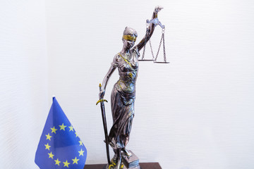 Statuette of Justice - Themis, ancient Greek goddess of divine law & justice. EU flag is on the table is next.