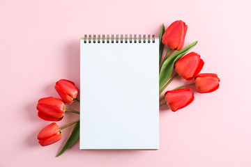 Notebook with space for text and beautiful red tulips on color background