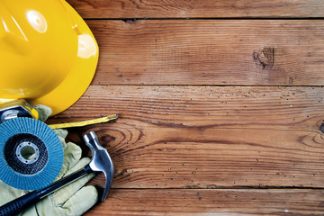 hammer, protective gloves, grinding disc, roulette and yellow safety helmet on wooden background