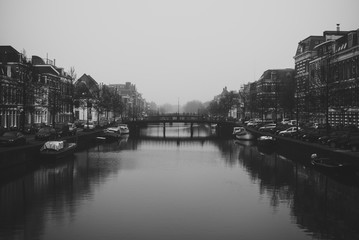 Fototapeta premium Charming cityscape of old Dutch town Haarlem. Stone bridge connecting two banks of the Spaarne river. Beautiful perspective. Misty and cloudy early spring weather. Black and white