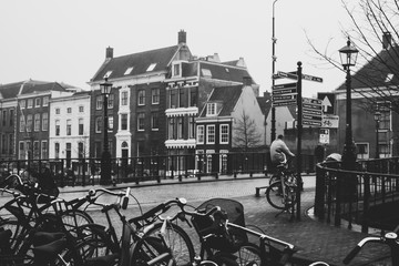An elderly man riding a biking and crossing the bridge in Harlem, Netherlands. Cyclist riding near bicycle parking lot. Vintage black and white colors.