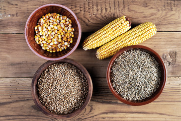 Maize, wheat, rye, meal and ceramic bowls on wooden table