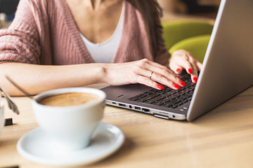 Attractive young woman sits at a table in a cafe with a cup of coffee and enjoys a laptop