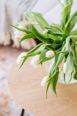 White tulips in a vase on a white table on a bright background