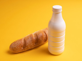 A bottle of milk or kefir baguette or loaf on a yellow background