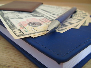  Money in a leather wallet with a notebook and a pen