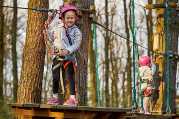 Two adorable little girls in helmet in a rope park in the woods