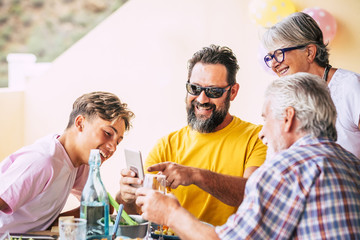 Family people three generations looking at mobile phone smiling together. Wood table with natural meal. Bright light