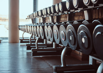 Photo of many different dumbbells in modern sunny gym.