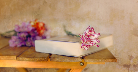 Un clavel rojo y blanco posado sobre un libro con un ramo de flores al fondo