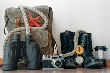 A backpack, binoculars, compass, pocket watch, rope and photo camera on a floor on a white wall background . Travel or adventure background.