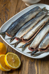 Raw saury on a white dish in the form of fish with lemon and herbs top view