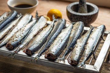 Raw saury on a grill for smoking with lemon and herbs top view