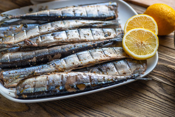 Smoked saury on a white dish in the form of fish with lemon and herbs