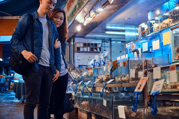 Young asian couple looking for something special at traditional chainese market. They are pensive. A lot of seafood at background.