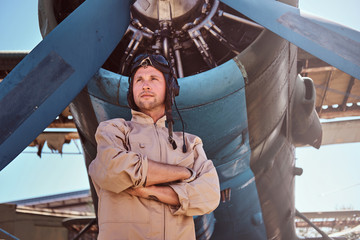 Military young pilot is thoughtfully looking up. He is standing near small jet, just under the propeller.