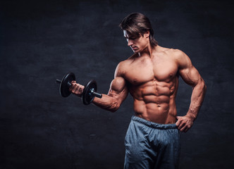 Fototapeta na wymiar Attractive shirtless bodybuilder is doing exercise with dumbbell. There is dark background.