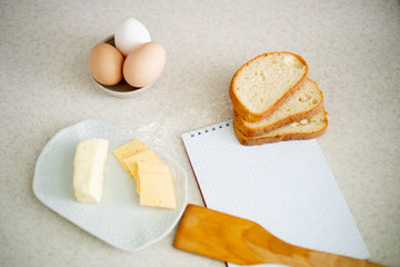 We cook breakfast. In the photo: flour, eggs, bread, cheese, notebook, olive oil, butter and wheat sprouts