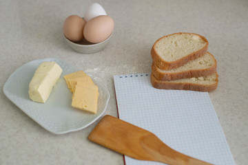We cook breakfast. In the photo: flour, eggs, bread, cheese, notebook, olive oil, butter and wheat sprouts