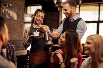 Two happy waiters serving fresh coffee to customers in coffee shop.