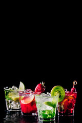 Four colorful tasty alcoholic cocktails in a row at the bar stand. Luxury vacation concept. Place for text. Vertical, isolated on black