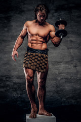 Bautiful strong bodybuilder is posing on white pedestal with naked torso, dumbbell and gladiator's bandage.