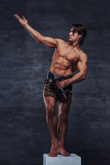 Beautiful strong bodybuilder is posing on white pedestal with naked torso, dumbbell and gladiator's bandage.