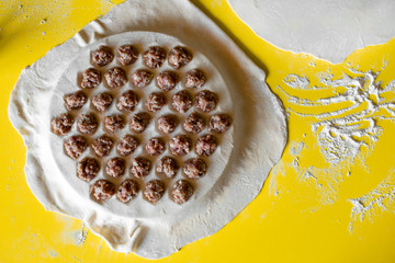 process of cooking meat dumplings stuffed on the dough top view on a yellow table.
