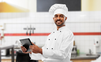 cooking, technology and people concept - happy male indian chef in toque with tablet computer over restaurant kitchen background