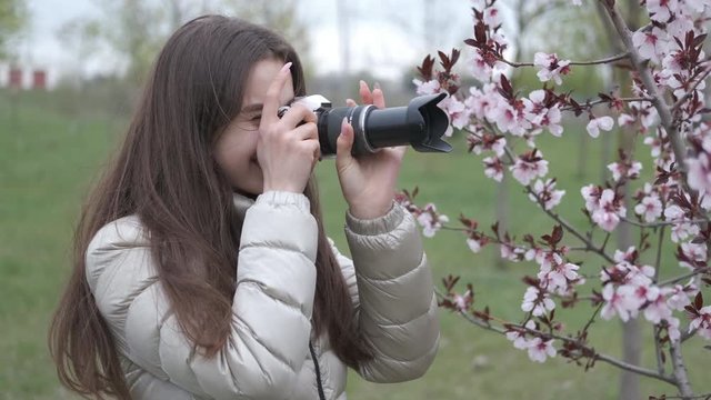 Girl with a camera in the spring. Young photographer. A charming little girl takes pictures of the spring flowering trees.