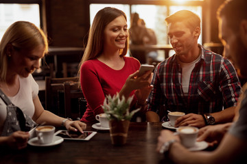 Happy couple using cell phone while being with friends in a cafe.